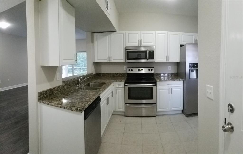 A kitchen features white cabinets, granite countertops, stainless steel appliances, and tile flooring — 6012 PORTSDALE PLACE UNIT 101, RIVERVIEW, FL