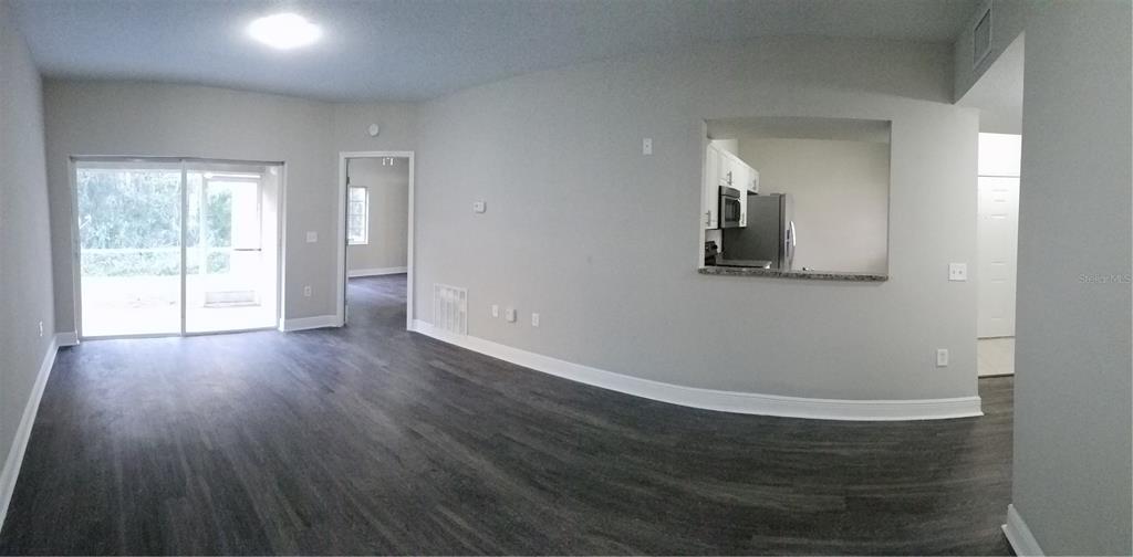 A living area with gray wood-look flooring, a sliding glass door, and a kitchen pass-through — 6012 PORTSDALE PLACE UNIT 101, RIVERVIEW, FL
