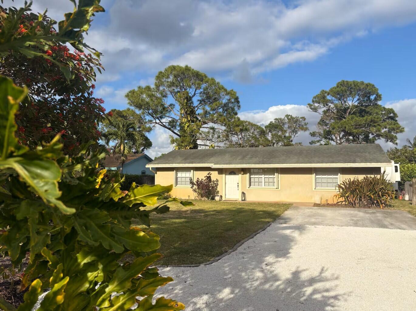 A single-story tan house with a gravel driveway and a large tree in the yard — 5586 3rd Road, Lake Worth FL 33467, LAKE WORTH, FL
