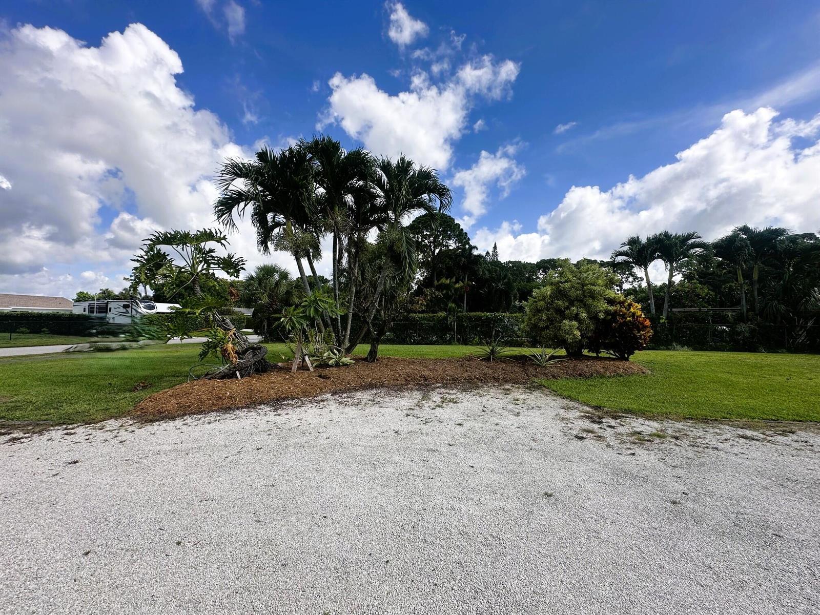 A gravel driveway leads to a landscaped garden bed with palm trees and green lawn — 5586 3rd Road, Lake Worth FL 33467, LAKE WORTH, FL