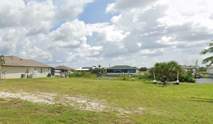 A grassy vacant lot sits in front of a canal with neighboring houses in the background — 1707 NW 44TH AVENUE, CAPE CORAL, FL