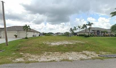 A vacant residential lot sits between two houses under a cloudy sky — 1707 NW 44TH AVENUE, CAPE CORAL, FL