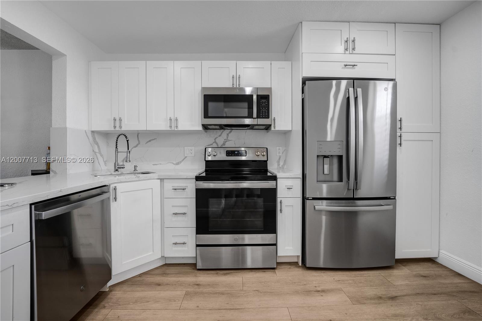 A modern kitchen features white cabinets, stainless steel appliances, and marble-patterned countertops and backsplash — 2551 Aragon Blvd # 411, Sunrise FL 33322, SUNRISE, FL