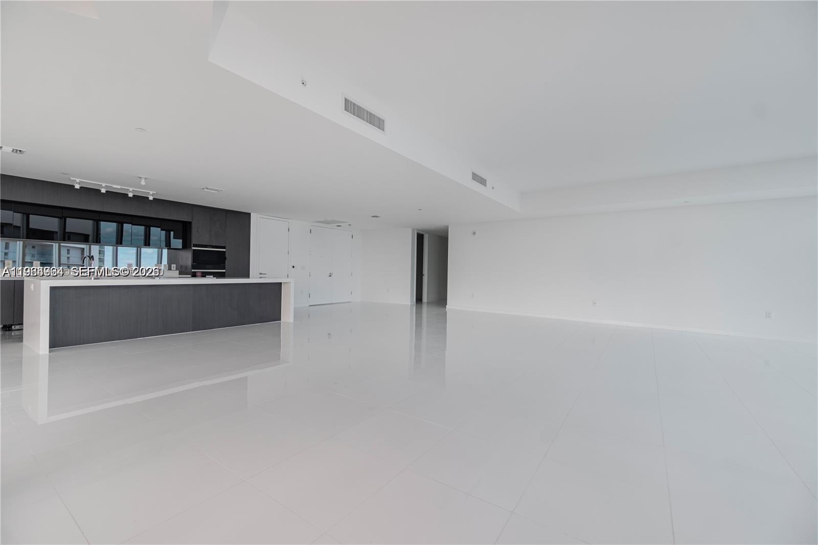 A modern, open-concept living area features white tile floors, white walls, and a dark kitchen — 851 NE 1st Ave # 4911, Miami FL 33132, MIAMI, FL