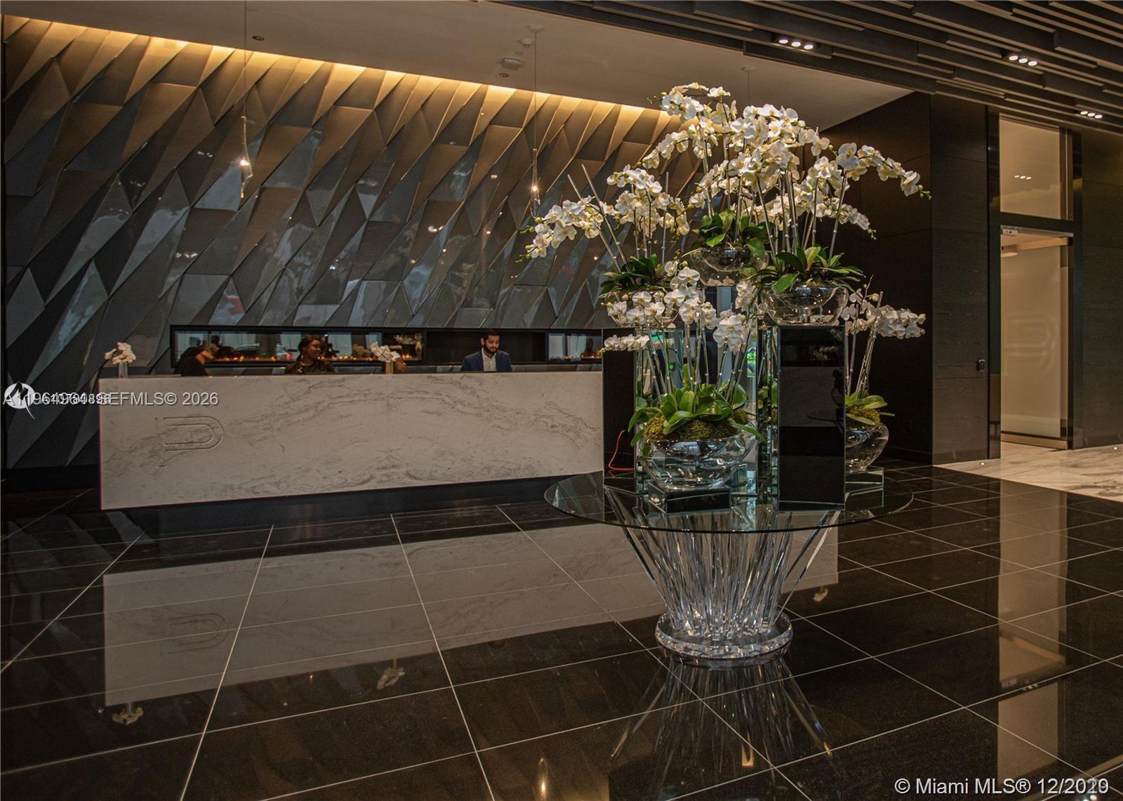 A modern lobby features a marble reception desk, black tiled floors, and a large floral arrangement — 851 NE 1st Ave # 4911, Miami FL 33132, MIAMI, FL
