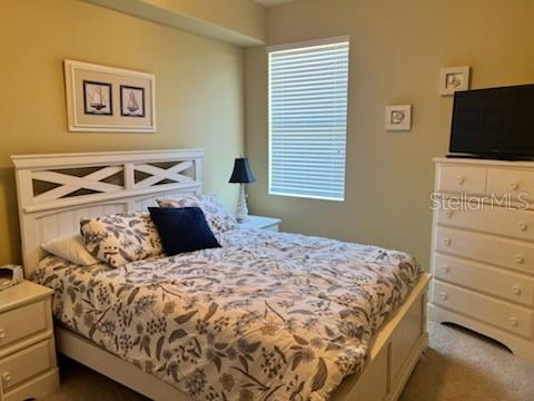 A bedroom features a white bed frame, floral bedding, a dresser with a television, and blinds — 8406 GRAND ESTUARY TRAIL UNIT 104, BRADENTON, FL