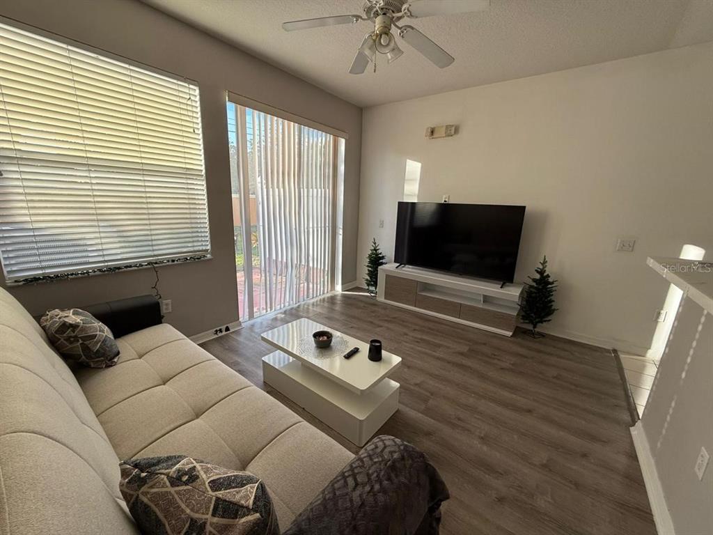 A living room features light wood-look flooring, a sofa, a coffee table, and a television — 5210 PARADISE CAY CIRCLE, KISSIMMEE, FL