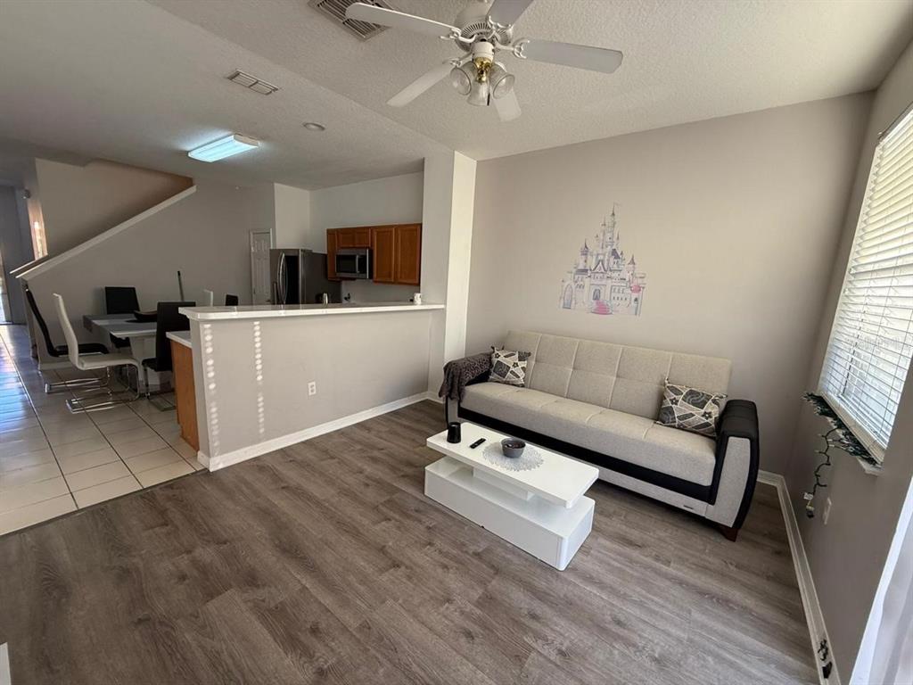 A living room with wood-look flooring, a grey sofa, and an open kitchen with bar seating — 5210 PARADISE CAY CIRCLE, KISSIMMEE, FL