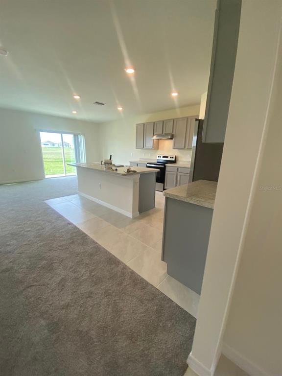 A kitchen with gray cabinets and a central island overlooks a carpeted living area — 701 SILVER PALM DRIVE, HAINES CITY, FL