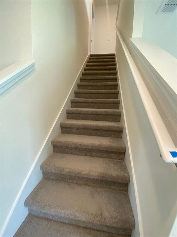 A straight staircase with brown carpeted steps and white walls leads to an upper landing — 701 SILVER PALM DRIVE, HAINES CITY, FL