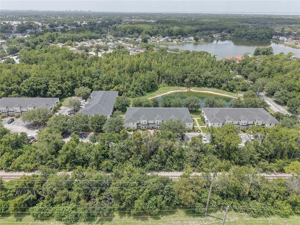 An aerial view shows several multi-story apartment buildings surrounded by dense trees and a pond — 9516 CHARLESBERG DRIVE, TAMPA, FL
