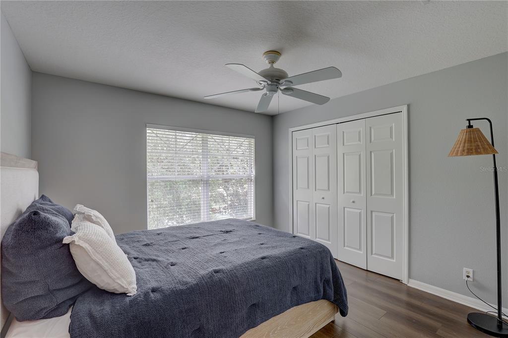 A bedroom features a bed with a blue quilt, a ceiling fan, and white closets — 9516 CHARLESBERG DRIVE, TAMPA, FL