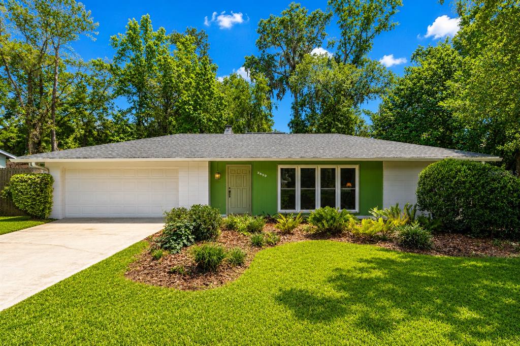 A single-story house with a green facade, white garage door, and a landscaped front yard — 3859 NW 32ND PL, GAINESVILLE, FL