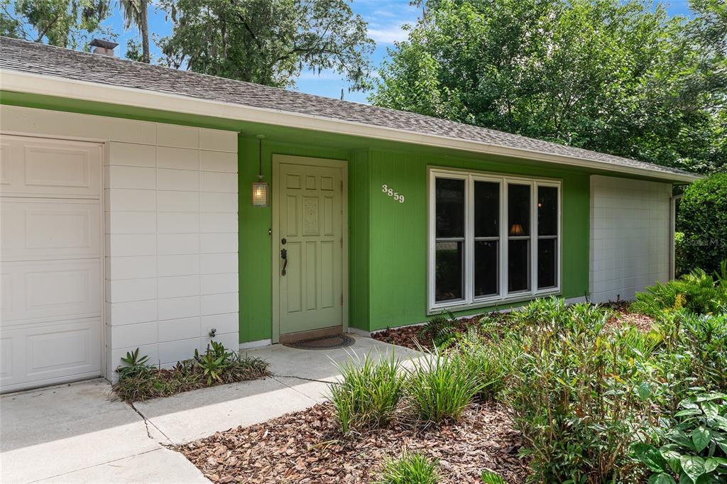 The exterior of a house features a green front door, white siding, and a large window — 3859 NW 32ND PL, GAINESVILLE, FL