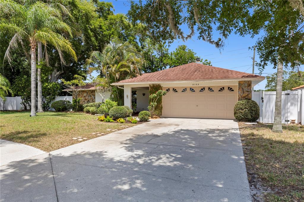 A single-story house with a tan garage, stone accents, and a palm tree in front — 3153 CARLOS DRIVE, DUNEDIN, FL