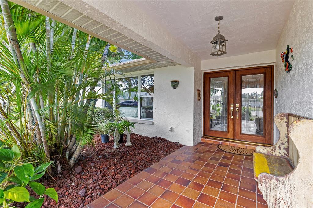 A covered porch features tiled flooring, a wooden double door, and a landscaped rock garden — 3153 CARLOS DRIVE, DUNEDIN, FL