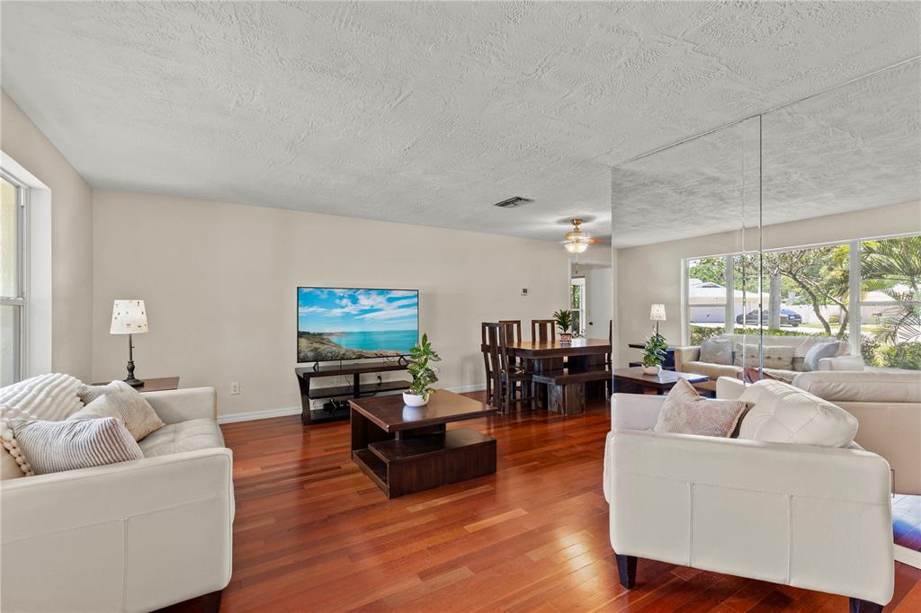 A living room with hardwood floors, white sofas, a television, and a mirrored wall — 3153 CARLOS DRIVE, DUNEDIN, FL