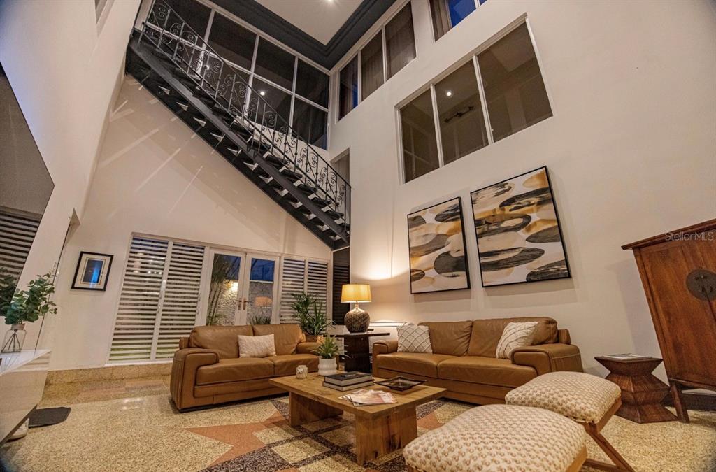 A high-ceilinged living room features a metal staircase, two leather sofas, and large windows — 1375 MARGINAL VILLAMAR, CAROLINA, PR