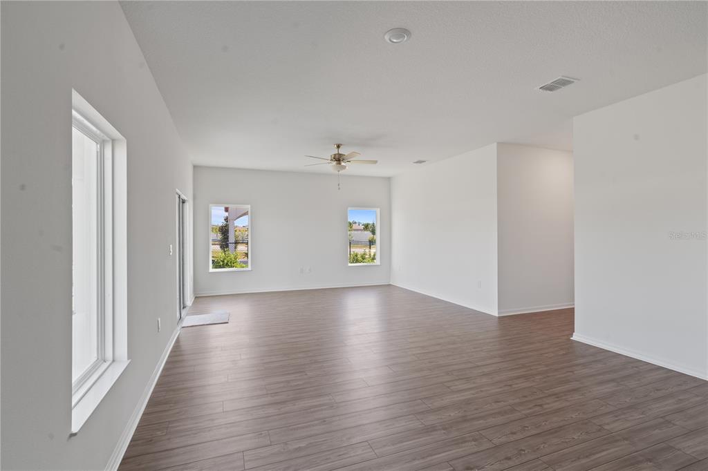 An empty living area features white walls, wood-look flooring, a ceiling fan, and large windows — 1774 WHITE ELEPHANT LOOP, WINTER HAVEN, FL