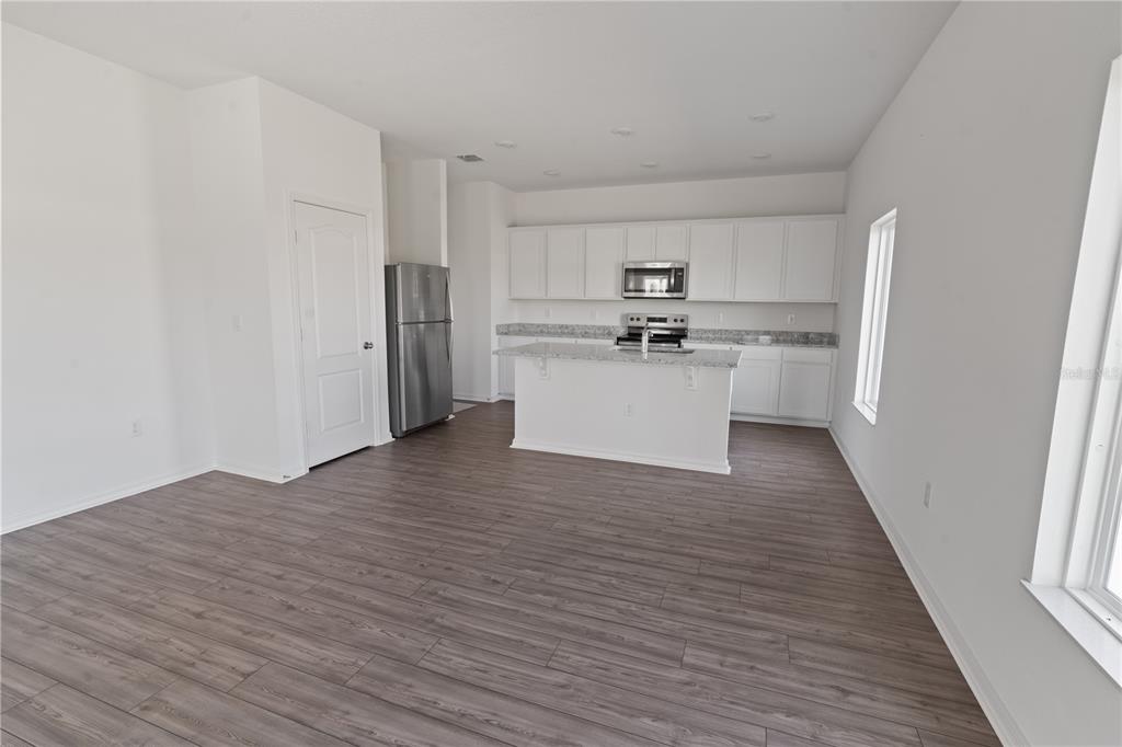 A kitchen with white cabinets, stainless steel appliances, a center island, and wood-look flooring — 1774 WHITE ELEPHANT LOOP, WINTER HAVEN, FL