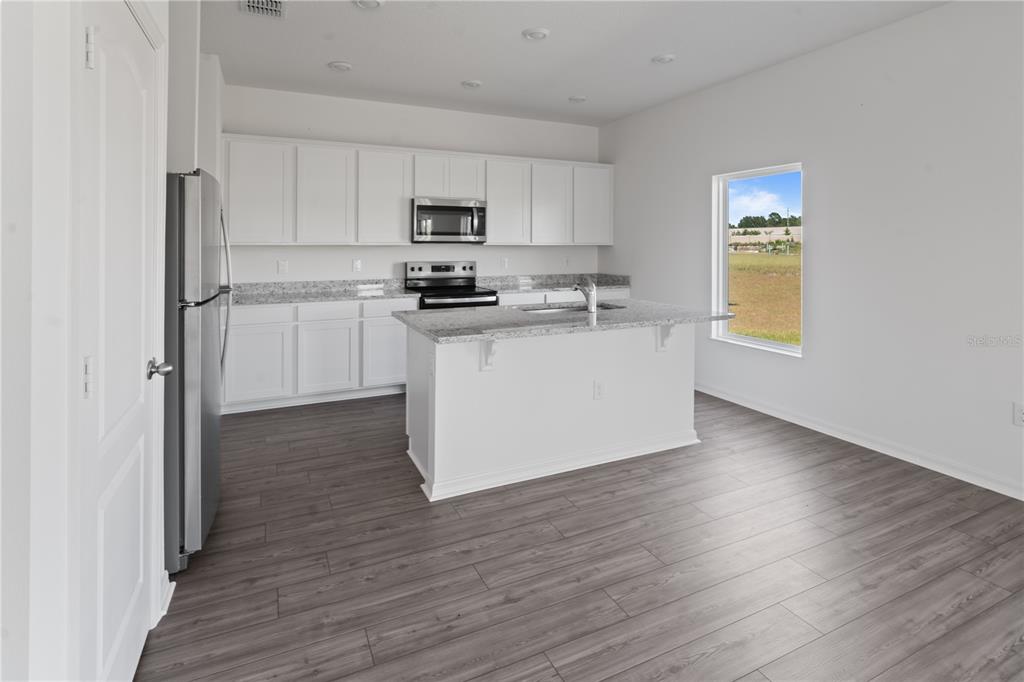 A kitchen with white cabinets, granite countertops, a center island, and gray wood-look flooring — 1774 WHITE ELEPHANT LOOP, WINTER HAVEN, FL