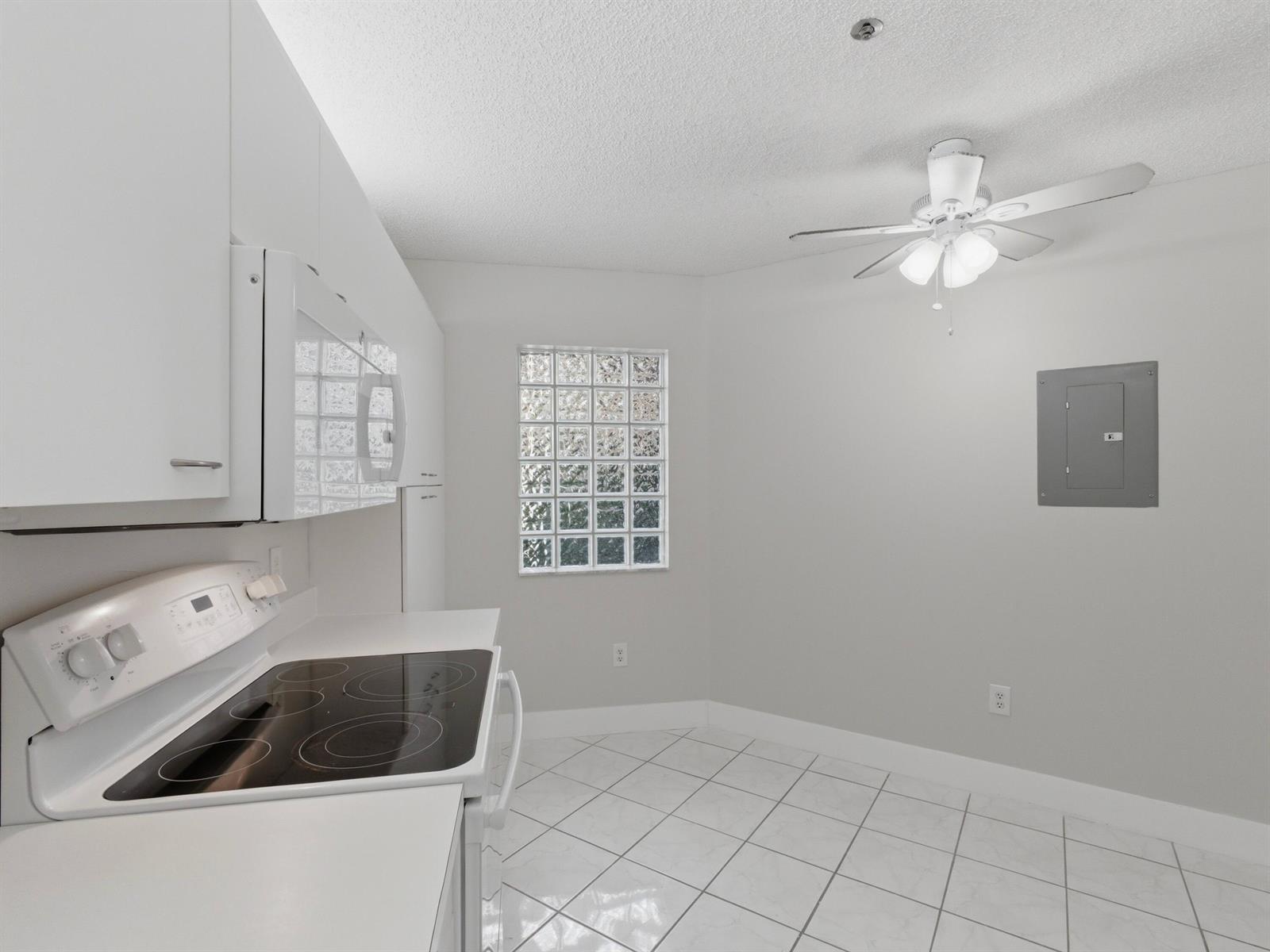 A white kitchen features tile flooring, a glass block window, and a ceiling fan — 5265 Brisata Circle # P, Boynton Beach FL 33437, BOYNTON BEACH, FL