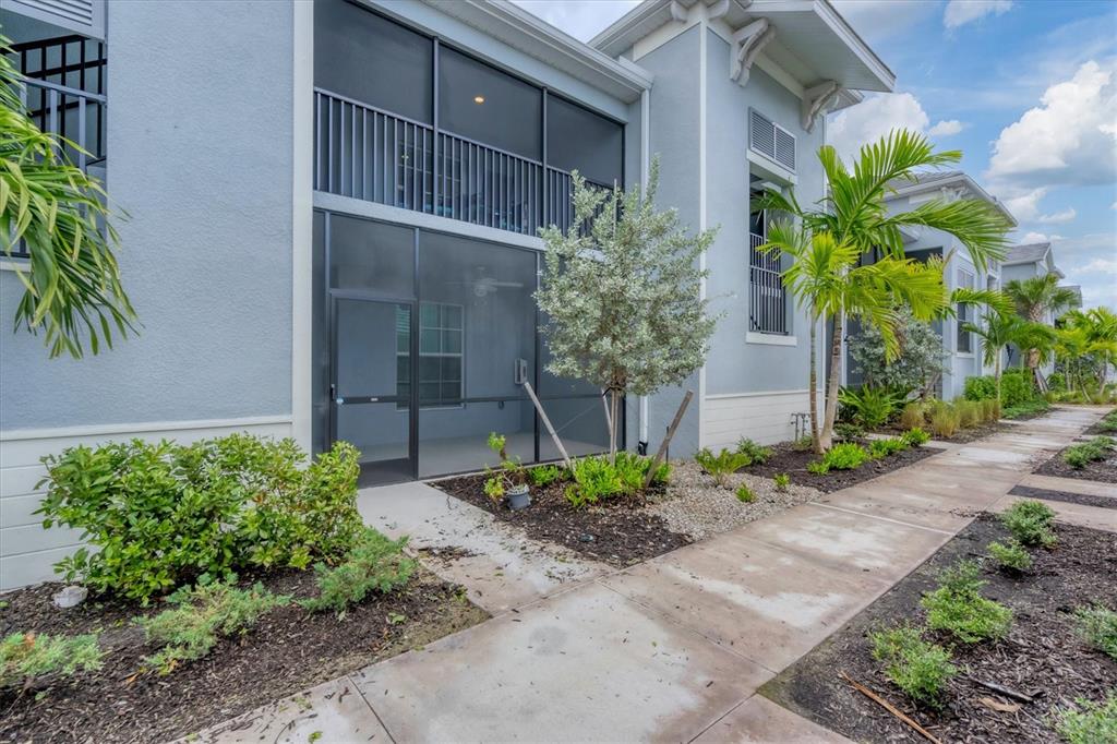 A ground-level screened-in patio sits beside a sidewalk and landscaped garden area — 14224 HEIRTAGE LANDING BOULEVARD UNIT 921, PUNTA GORDA, FL