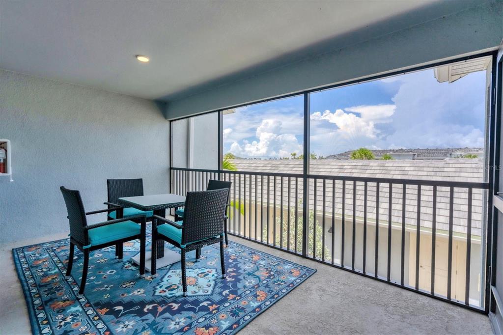 A screened-in balcony features a small table with four chairs on a patterned blue rug — 14224 HEIRTAGE LANDING BOULEVARD UNIT 921, PUNTA GORDA, FL