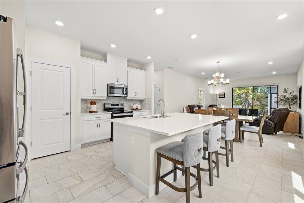 A modern kitchen features white cabinetry, a central island with bar seating, and tile flooring — 1309 LOMBARDI COURT, KISSIMMEE, FL