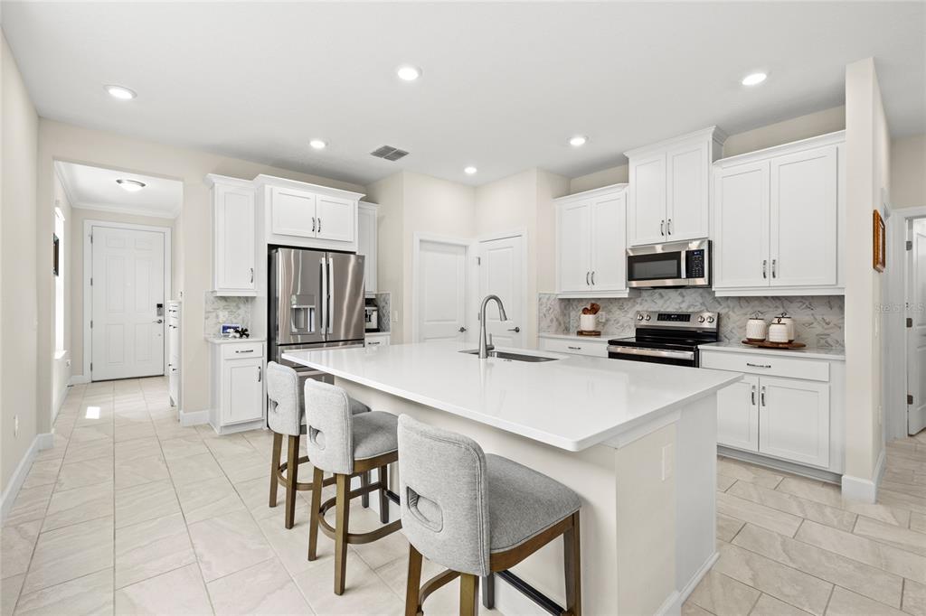 A kitchen with white cabinets, a large quartz island, stainless steel appliances, and tile flooring — 1309 LOMBARDI COURT, KISSIMMEE, FL
