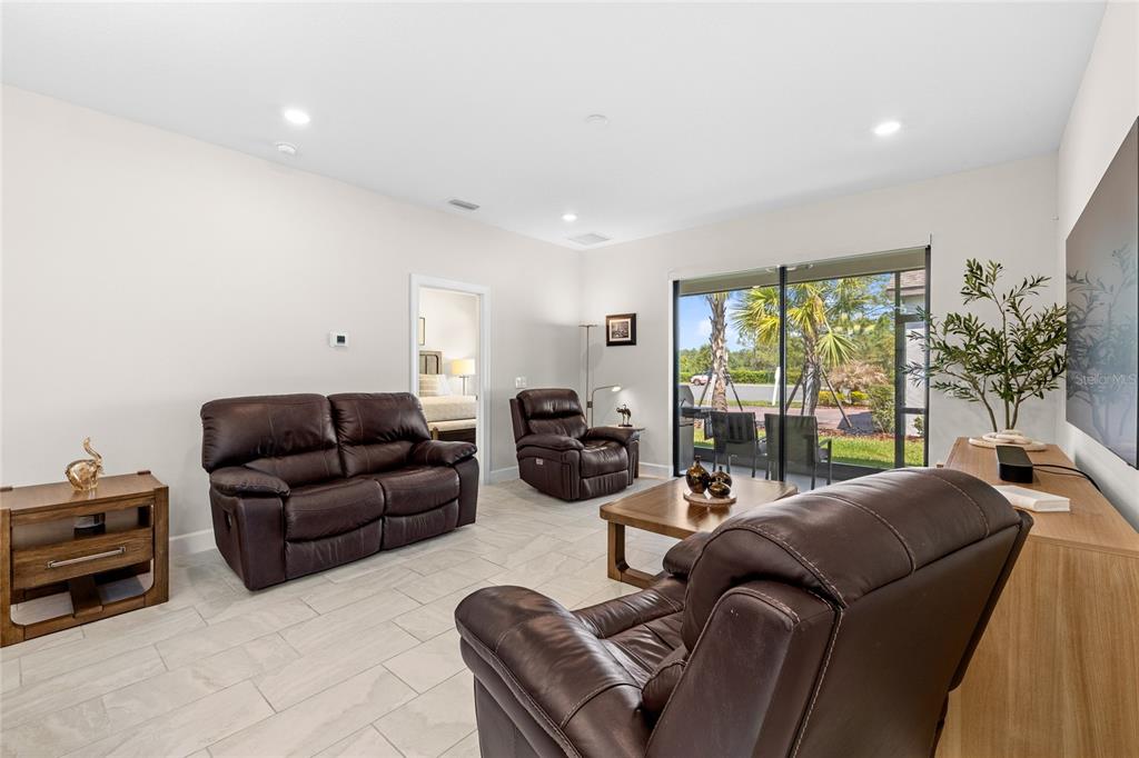A living room features brown leather furniture, tile flooring, and sliding glass doors to a patio — 1309 LOMBARDI COURT, KISSIMMEE, FL