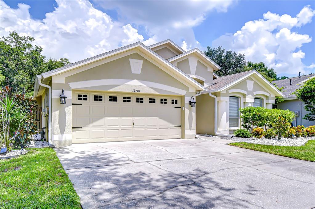 A single-story house with a beige stucco exterior, a two-car garage, and a concrete driveway — 19707 ELLENDALE DRIVE, LAND O LAKES, FL
