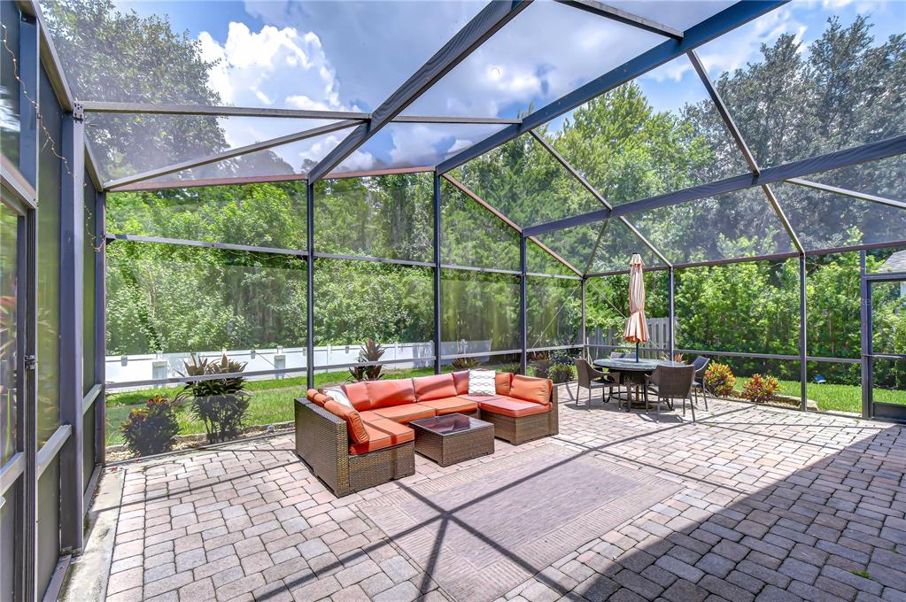 A screened-in patio features a brick paver floor, outdoor sectional seating, and a dining set — 19707 ELLENDALE DRIVE, LAND O LAKES, FL