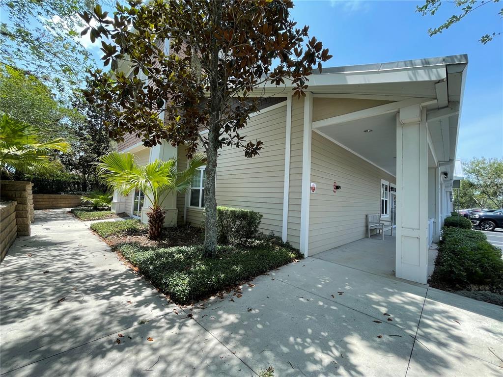 A beige building exterior features a covered walkway, a small palm tree, and landscaping — 757 HWY  466 UNIT 100, LADY LAKE, FL
