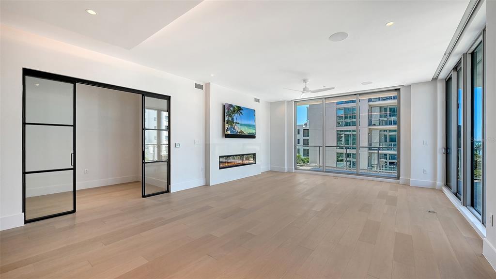 A bright living room features light wood floors, a fireplace, and black-framed glass doors — 253 GOLDEN GATE POINT UNIT 401, SARASOTA, FL