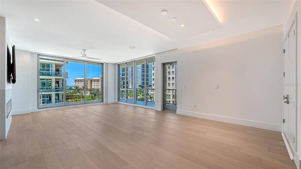 A spacious, unfurnished living room features light wood flooring, floor-to-ceiling windows, and a ceiling fan — 253 GOLDEN GATE POINT UNIT 401, SARASOTA, FL