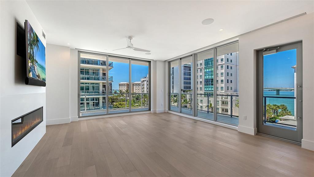 A modern living room with light wood floors, a fireplace, and floor-to-ceiling windows overlooking water — 253 GOLDEN GATE POINT UNIT 401, SARASOTA, FL