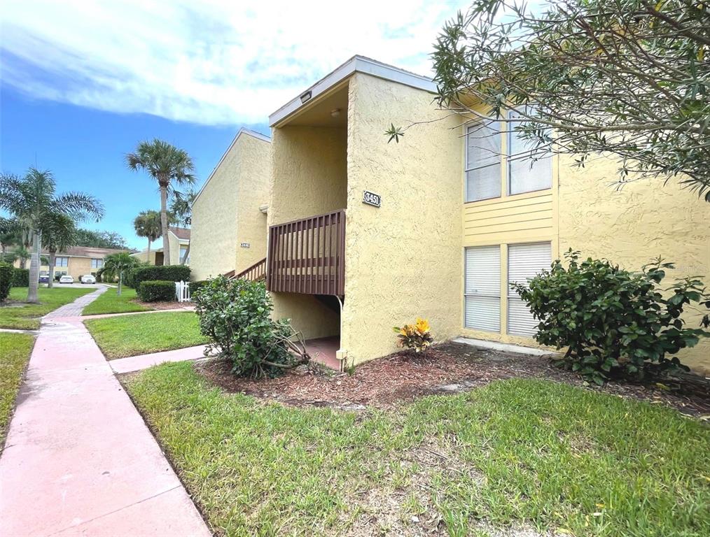 A two-story yellow stucco apartment building features a wooden balcony and a paved walkway — 3451 CLARK ROAD UNIT 249, SARASOTA, FL