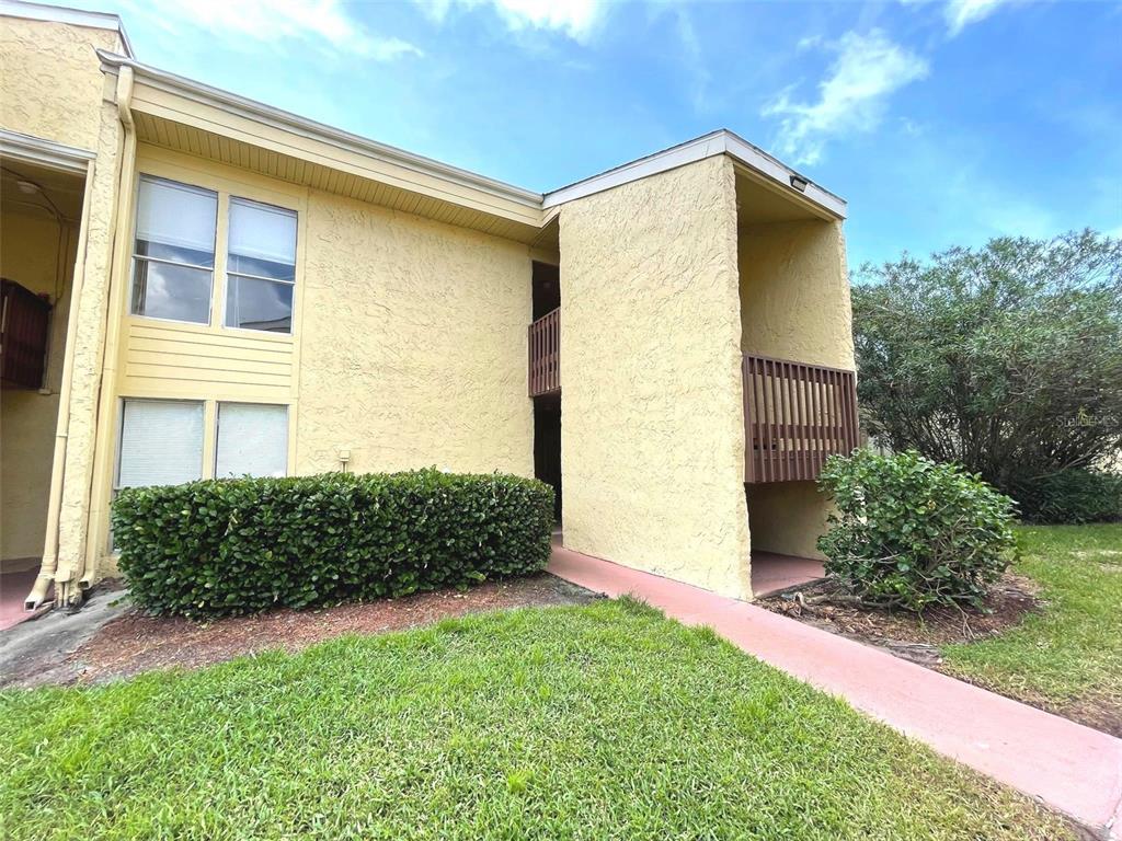 A two-story yellow stucco building features a ground-level walkway, a balcony, and a manicured hedge — 3451 CLARK ROAD UNIT 249, SARASOTA, FL