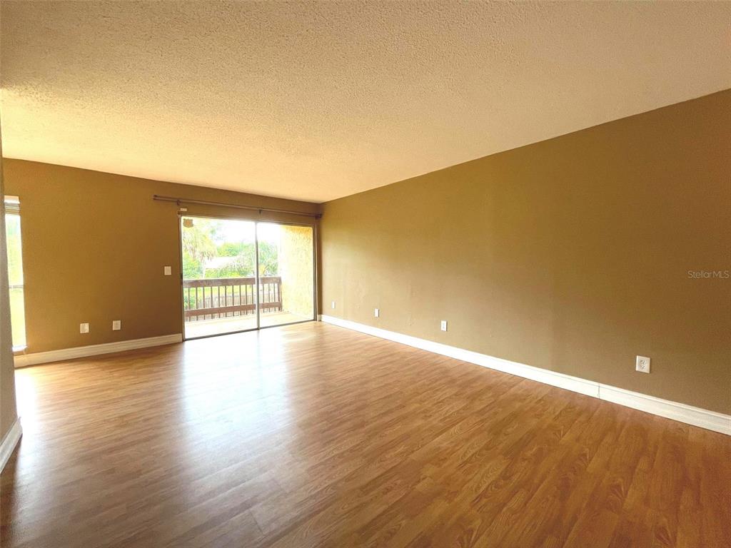 An empty living room features tan walls, wood-look flooring, and a sliding glass door — 3451 CLARK ROAD UNIT 249, SARASOTA, FL