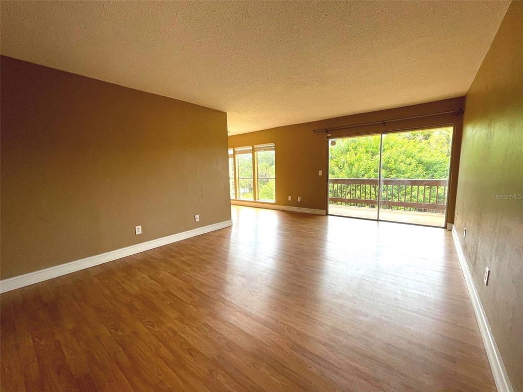 An empty living room features wood-look flooring, tan walls, and a sliding glass balcony door — 3451 CLARK ROAD UNIT 249, SARASOTA, FL