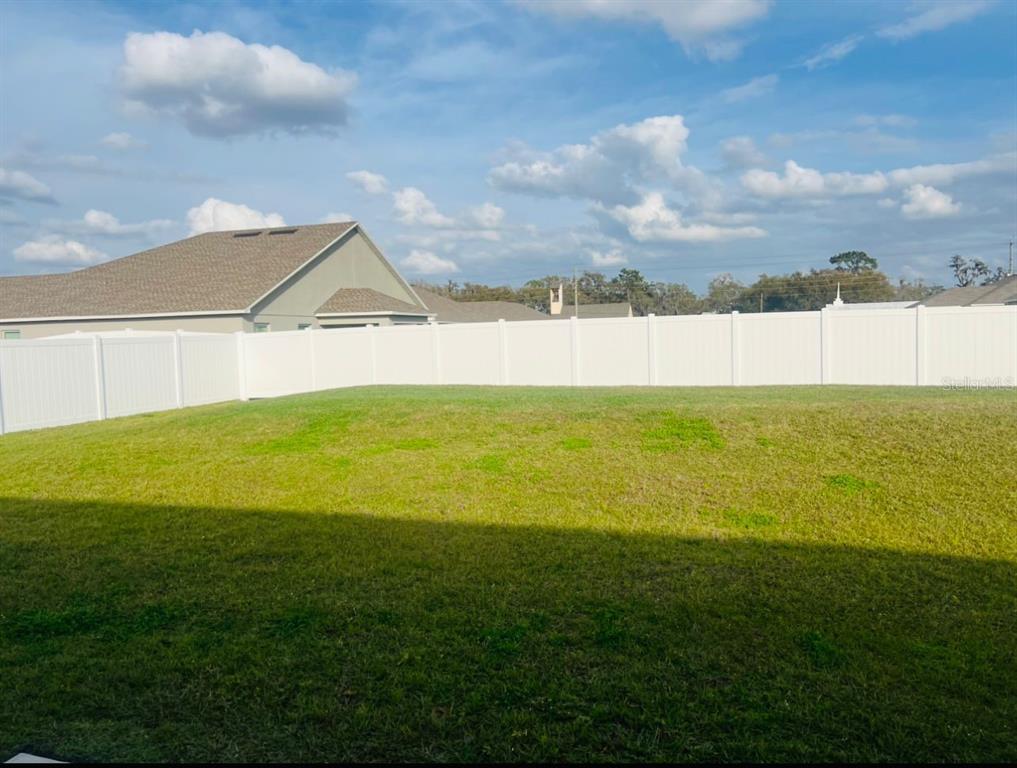 A grassy backyard features a white vinyl privacy fence under a blue sky — 2713 HUDSON STREET, LAKELAND, FL