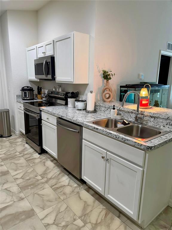 A kitchen features white cabinets, granite countertops, stainless steel appliances, and marble-patterned tile flooring — 2713 HUDSON STREET, LAKELAND, FL