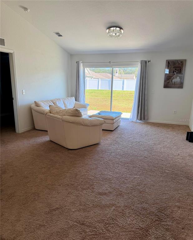 A living room features beige carpet, white walls, a white sofa, and sliding glass doors — 2713 HUDSON STREET, LAKELAND, FL