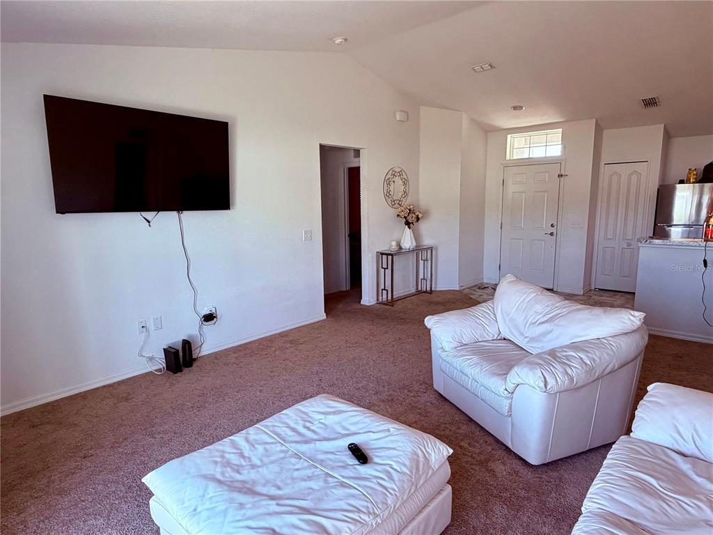 A living room features a wall-mounted television, white furniture, and beige carpet — 2713 HUDSON STREET, LAKELAND, FL