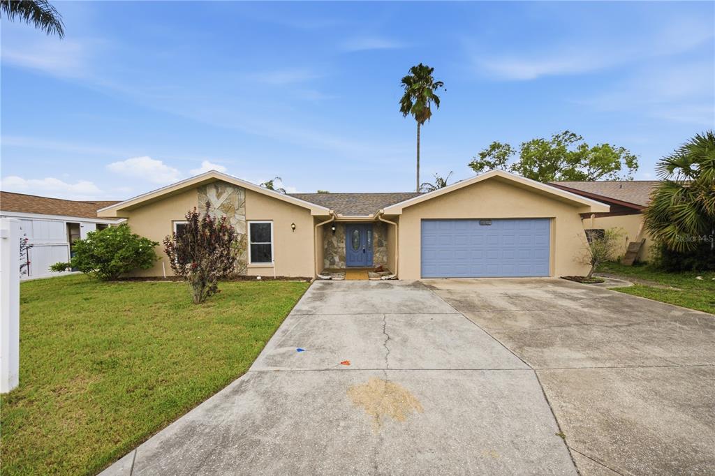 A single-story house with a tan exterior, stone accents, a blue door, and a two-car garage — 9840 SAN SEBASTIAN WAY, PORT RICHEY, FL