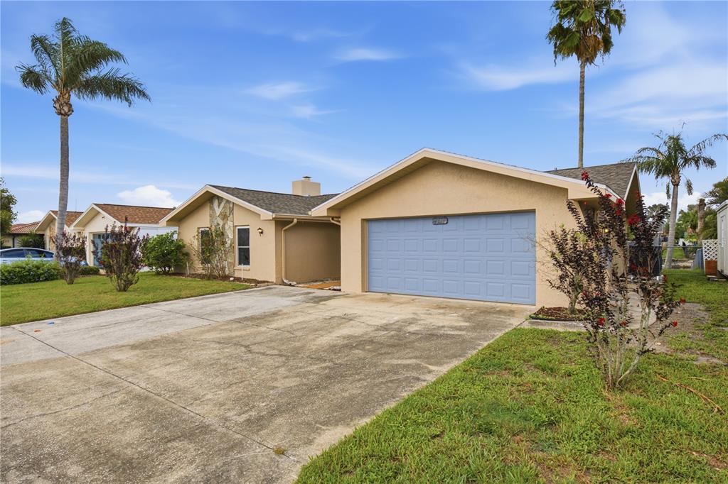 A single-story house with a light-colored exterior, a blue garage door, and palm trees — 9840 SAN SEBASTIAN WAY, PORT RICHEY, FL