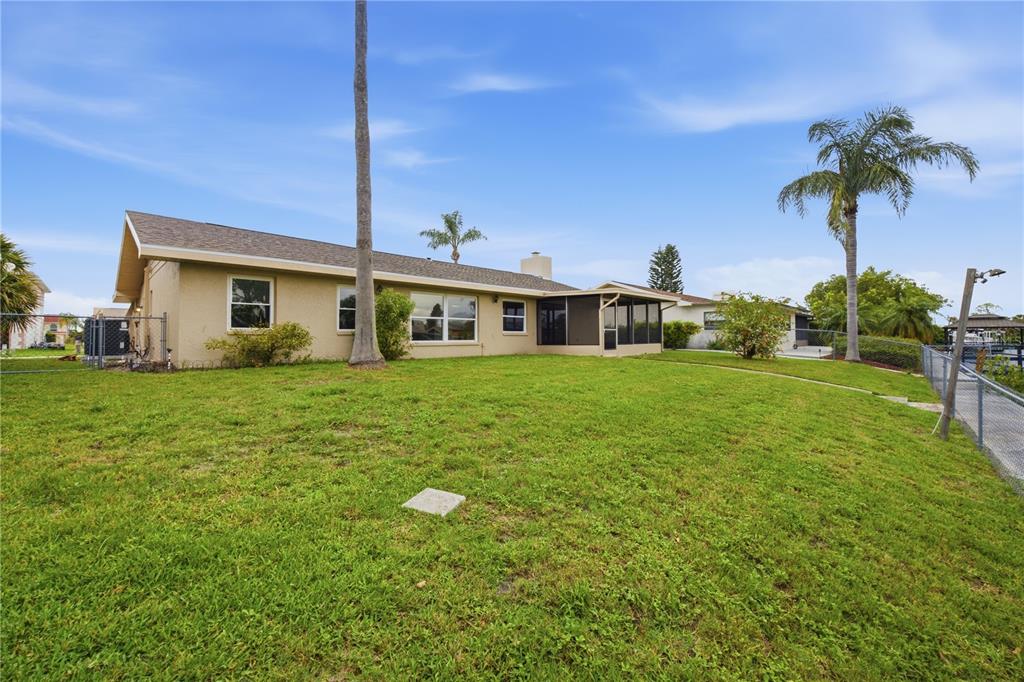 The exterior of a single-story house features a screened-in porch and a large grassy yard — 9840 SAN SEBASTIAN WAY, PORT RICHEY, FL
