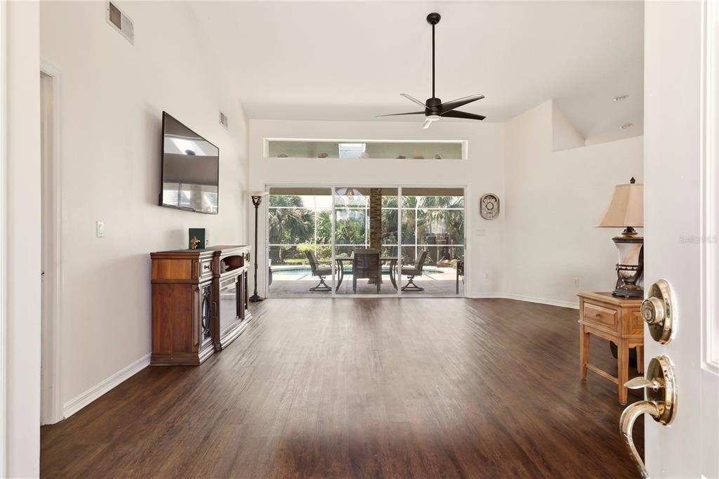 A living room with dark wood floors, a ceiling fan, and sliding doors to a pool — 4 BEACHSIDE DR, PALM COAST, FL