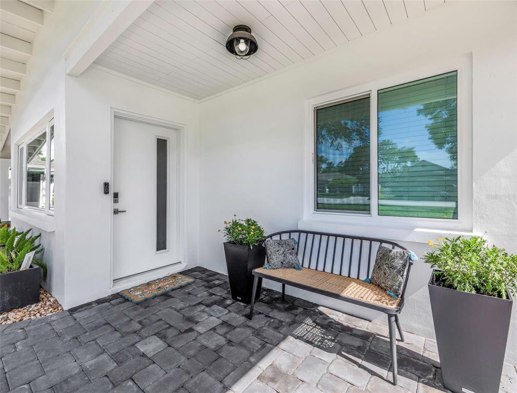 A white front door and a metal bench sit on a paved patio entrance — 1109 MARINE STREET, CLEARWATER, FL